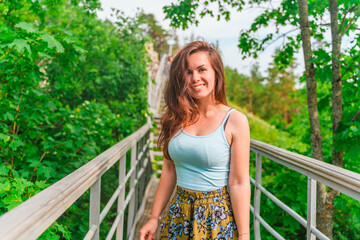 Portrait of a cute young woman on a bridge in the mountains in a dense forest. Picturesque summer green background - Powered by Adobe