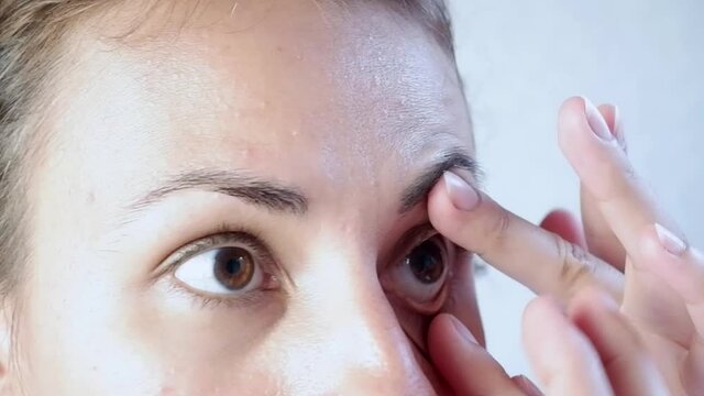 Close-up of a woman removing soft contact lenses from her eye against a white background.