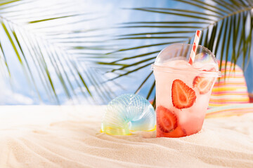 Cold fresh pink cocktail with ice, straw in plastic mug in sunlight on tropical beach with ocean view, sun hat, toy for children. Summer lifestyle and vacation on sea coast.