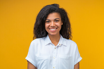 Close up portrait of young smiling attractive african american woman in white shirt, isolated over bright colored orange yellow background