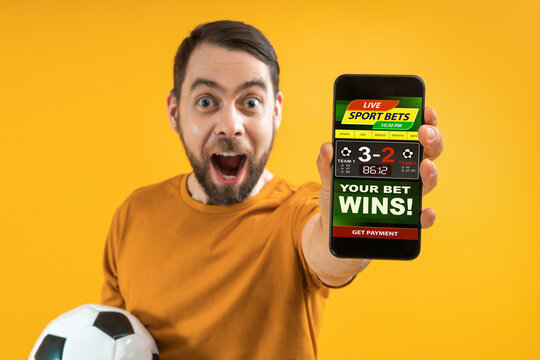 Image of euphoric football fan showing to the camera his smartphone with bookmaker's website application interface template