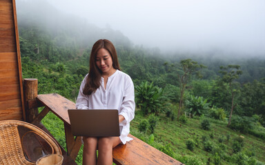 A woman using and working on laptop computer while sitting on balcony with a beautiful nature view on foggy day