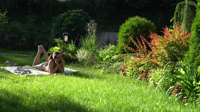 A woman liA woman lies on the lawn next to her house in the sun, surrounded by flowers.es on the lawn next to her house in the sun, surrounded by flowers. High quality 4k footage