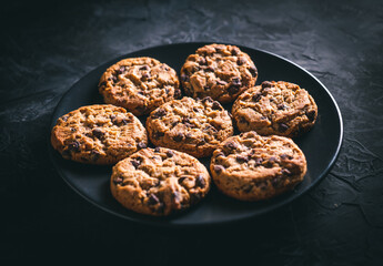 Homemade chocolate chip cookies on a black plate on a dark table. Ready to eat.