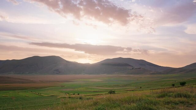 Time lapse: sunset over Castelluccio di Norcia highlands, Italy. The village perched on hill top over blooming agriculture fields, the famous colourful flowering plain in the Apennines
