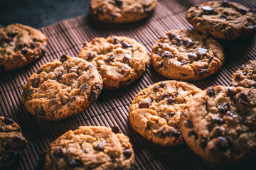 Homemade chocolate chip cookies on a brown wooden mat on a dark table. Ready to eat.