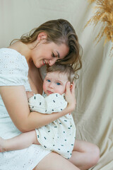 Beautiful young mother with blue-eyed little daughter on a beige background. Cozy.