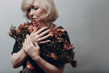 Upset elderly woman hold withered dry old rose flowers bouquet. Old age Concept.