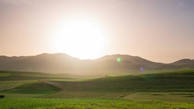 Time lapse: sunset over Castelluccio di Norcia highlands, Italy. The village perched on hill top over blooming agriculture fields, the famous colourful flowering plain in the Apennines