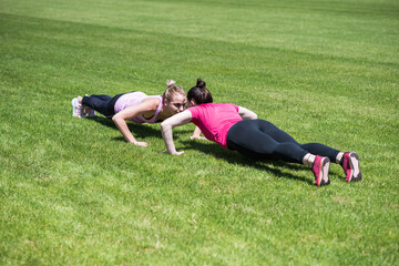 Fototapeta na wymiar Two women doing push-ups on the grass in the stadium. Practicing gym