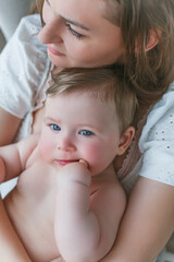 A beautiful young mother with a blue-eyed little daughter are resting at home. Cozy.