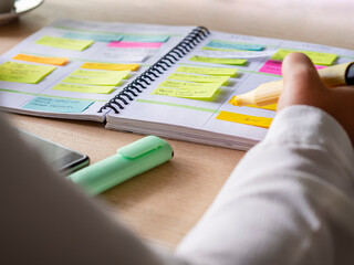 Close-up of agenda organize with color-coding sticky notes for time management. Productive schedule for appointments and reminders. Hand holding a yellow highlighter marker. Organization and planning - obrazy, fototapety, plakaty