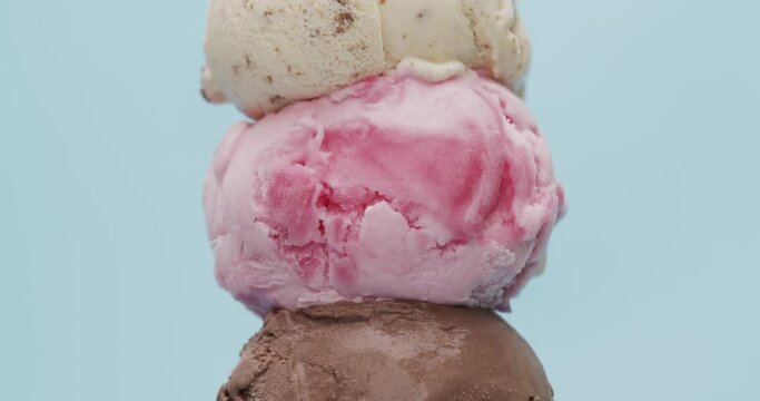 Close-up detail from bottom to top - Ice cream cones 3 flavors stacked Chocolate, strawberry, Chocolate Chip on blue background.