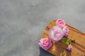 Summer refreshing drink of pink tea rose and ice cubes on wooden board on gray background, copy space