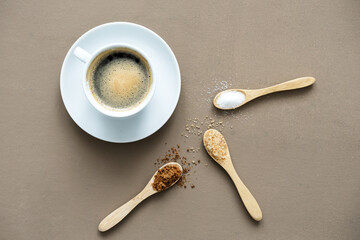 Eine Tasse Kaffee  und verschiedene Zuckerarten auf Holz Löffeln.. Draufsicht, brauner Hintergrund.