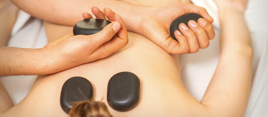 Obraz na płótnie Canvas Hot stone massage on the female back with hands of masseur holding black massage stones in spa salon