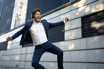 Business man wearing headphones in a blue suit, jumping in the street