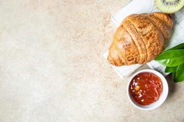 French croissant with jam and kiwi on light stone background. Tasty croissant. Top view.
