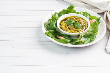 Pesto sauce in a plate and fresh basil leaves with garlic. copy space