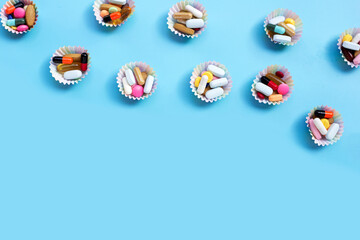 Colorful tablets with capsules and pills in cupcake wrappers on blue background.