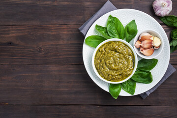 Pesto sauce in a plate and fresh basil leaves with garlic. dark wooden background, copy space.