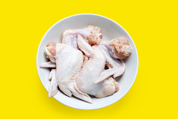 Fresh raw chicken wings in white bowl on yellow background.