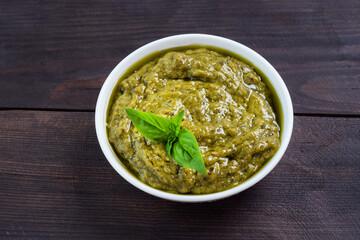 Pesto sauce in a plate and fresh basil leaves with garlic. dark wooden background, copy space.