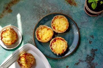 Mini quiches on a blue plate. Flaky dough pies. Fresh basil and mini quiches on a blue background. Direct sun shine.