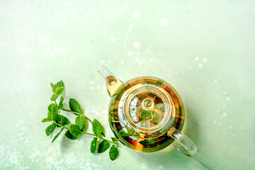 Glass teapot with tea and mint leaves on green table. Top view flat lay. Mint leaves with teapot on...
