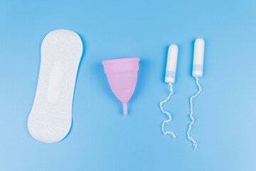 Sanitary pad, tampons and menstrual cup on blue background. Top view. Concept of critical days, menstruation, feminine hygiene