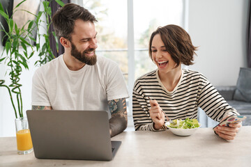 Beautiful couple sitting at the kitchen with laptop