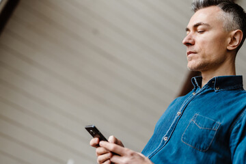 Mid aged casual man holding mobile phone