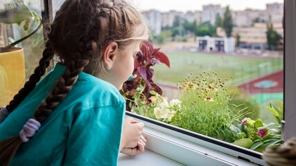 Cute girl helping to care for home plants on the balcony window, plant parents concept, home gardening, green environment, nature and ecology at home