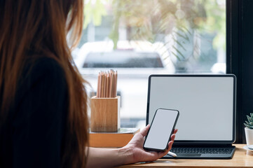 Cropped shot of woman hand holding blank screen smartphone while sitting at couonter table in cafe.