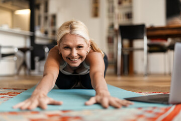 Blonde mature woman smiling and using laptop during yoga practice