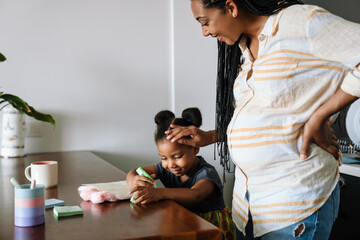 Black woman and her daughter smiling Black pregnant woman smiling while stroking her daughter's...