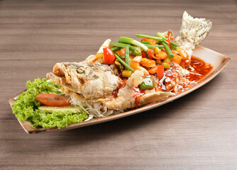 deep fried crispy whole grouper fish with vegetables in sweet and sour sauce on wood background asian halal menu