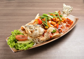 deep fried crispy whole grouper fish with vegetables in sweet and sour sauce on wood background asian halal menu