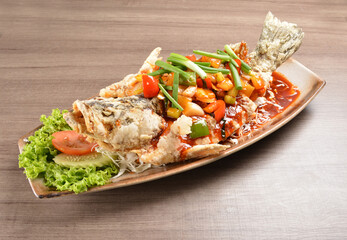 deep fried crispy whole grouper fish with vegetables in sweet and sour sauce on wood background asian halal menu