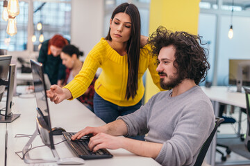 Fototapeta premium An attractive business girl standing next to a happy male colleague with clumsy hair and they are discussing new strategies in a modern office.