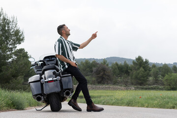 Chico sentado en una moto, señalando al cielo sonriente, en la naturaleza.