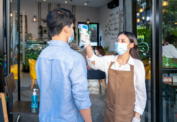 restaurant staff checking scan fever by digital thermometer to customer for protect infection coronavirus