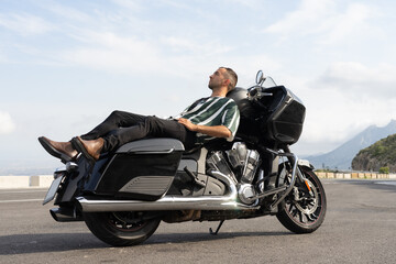 Fototapeta na wymiar Chico acostado en una moto negra en medio de la carretera con el cielo de fondo.