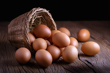 Brown chicken eggs in wicker basket on wooden table with dark background.