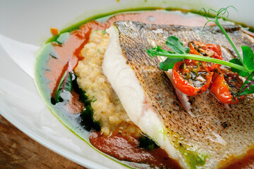 Fried fish fillet of halibut on a plate with tomato sauce. Cod or white fish with sauce and herbs, close-up