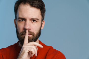 Brunette white man with beard smiling and showing silence gesture