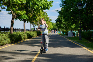 A 9-year-old boy is rolling on a scooter on the road in the park