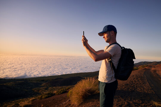 Concentrated man photographing landscape above clouds. Tourist enjoy at beautiful sunset. Tenerife, Canary Islands, Spain.