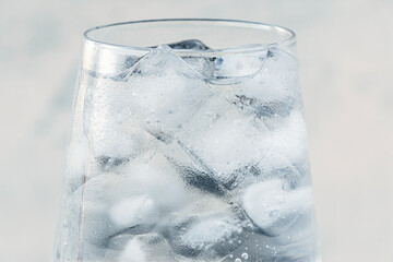 close up glass with ice water and ice cubes on white textured background. A refreshing and chilling drink in hot weather. soft focus