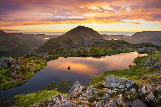Fantastic evening sunset over Lake District mountain range with reflections in water. Picturesque views from famous British landscape; Haystacks. Beauty in nature concept background.